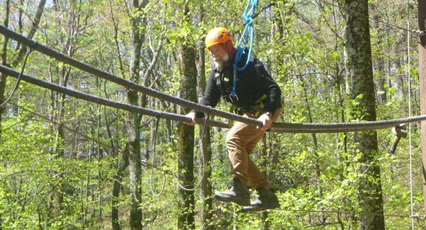 A person wearing safety gear is secured by ropes as they navigate a high ropes course. 